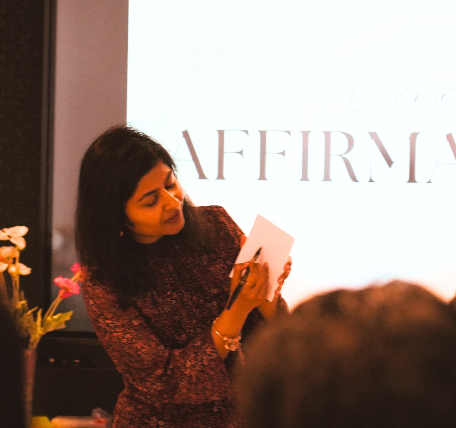 Woman holding a affirmation card in front of an audience with 'AFFIRMATION' displayed on a screen.